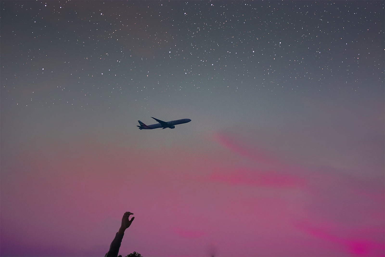 Hand reaching toward airplane seen high in the night sky.